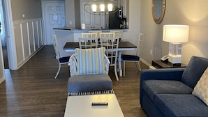 En moderne stue med en blå sofa, en stribet skammel og et spiseområde med bord og stole.