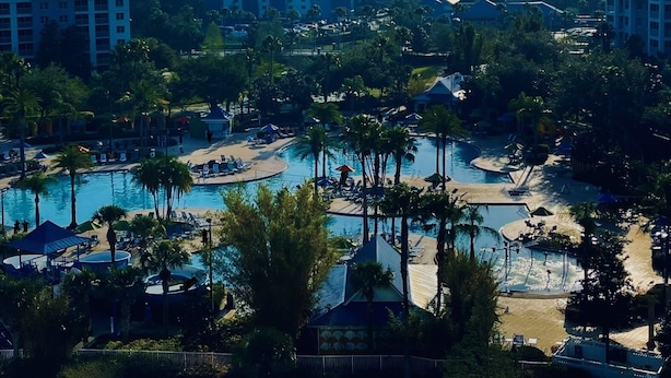 Et resort med en stor pool, palmer og flere bygninger i baggrunden.
