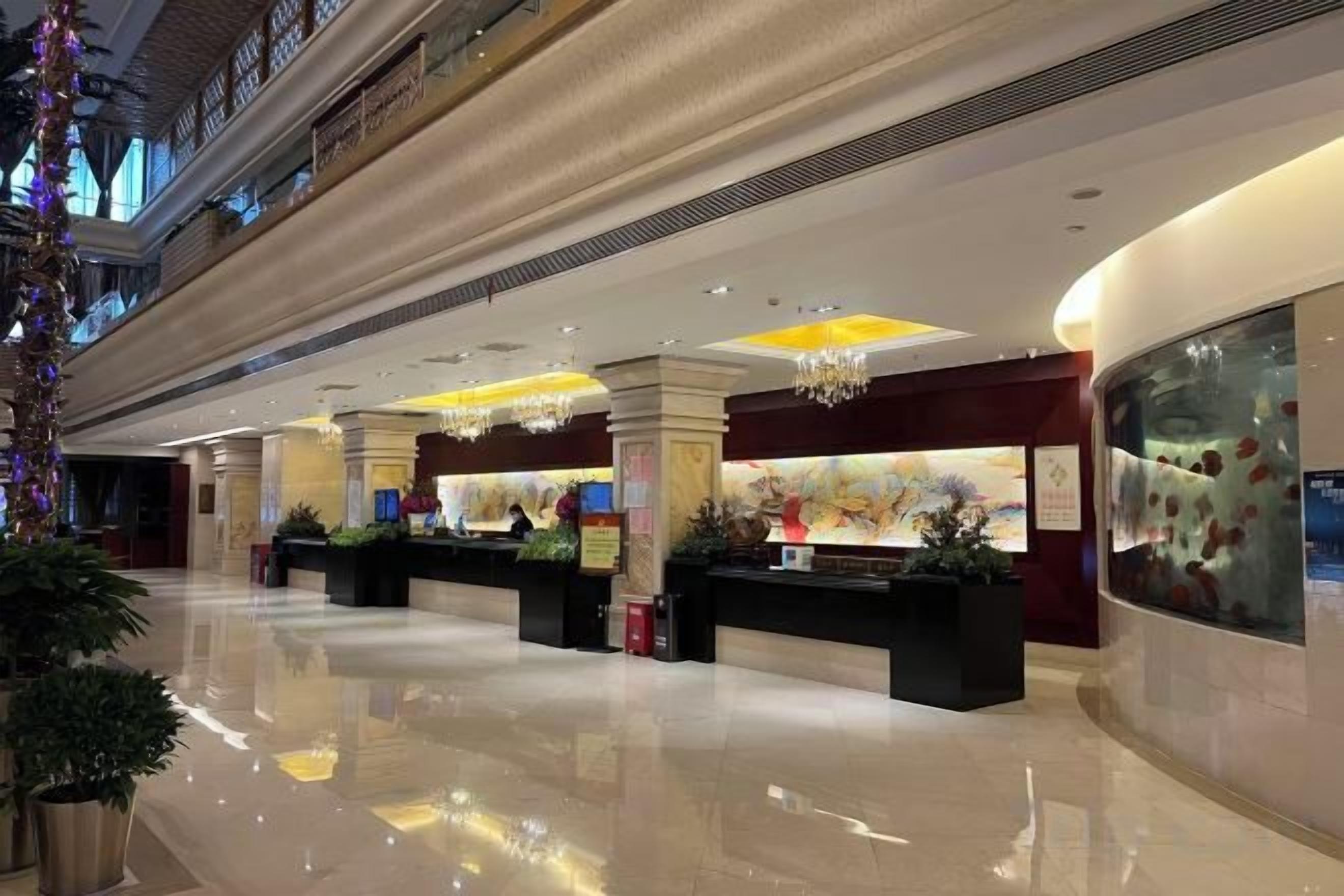 A hotel lobby with a reception desk, a large aquarium, and a high ceiling with decorative lighting.