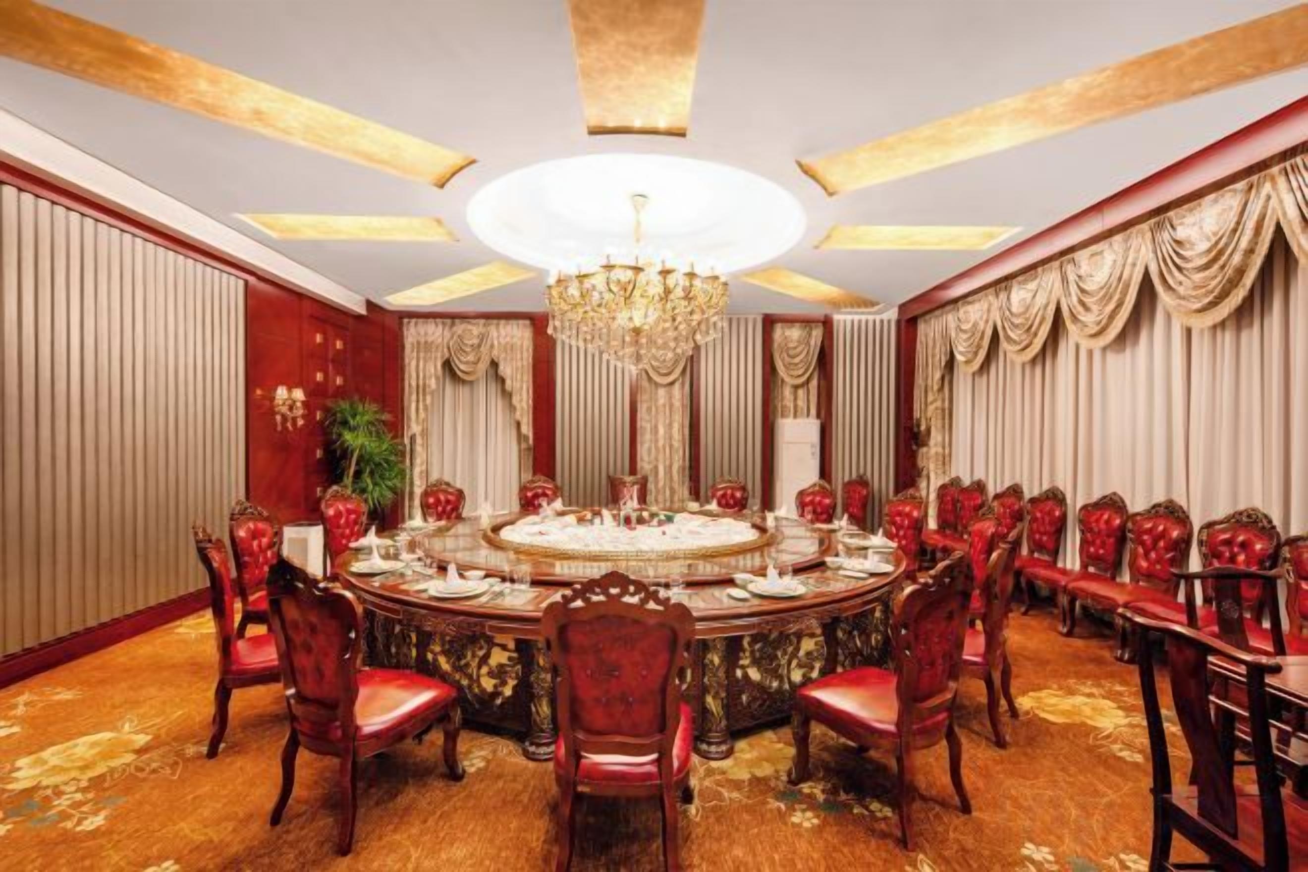 Uma sala de jantar formal com uma mesa redonda, cadeiras estofadas em vermelho e um candelabro.