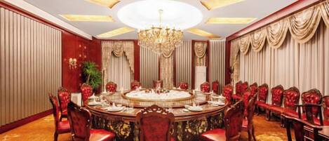 Uma sala de jantar formal com uma mesa redonda, cadeiras estofadas em vermelho e um candelabro.