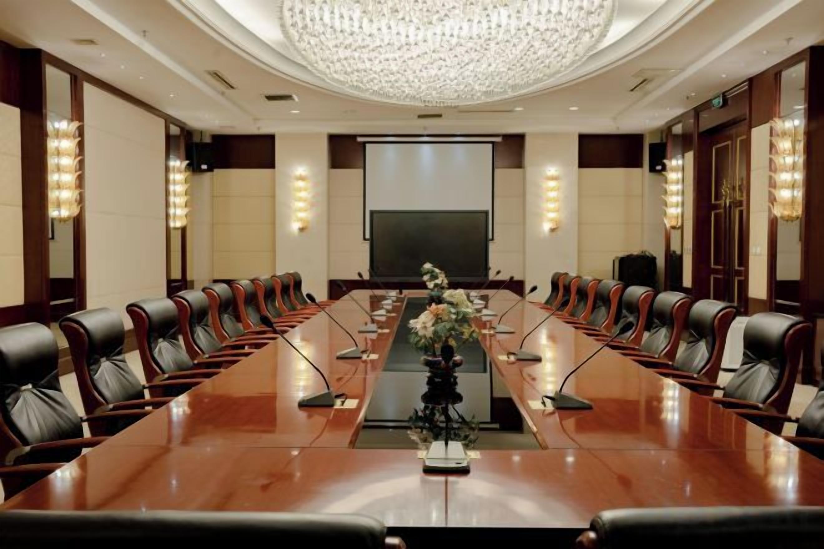 Un salón de conferencias con una larga mesa, sillas, una pantalla de proyector y una araña.