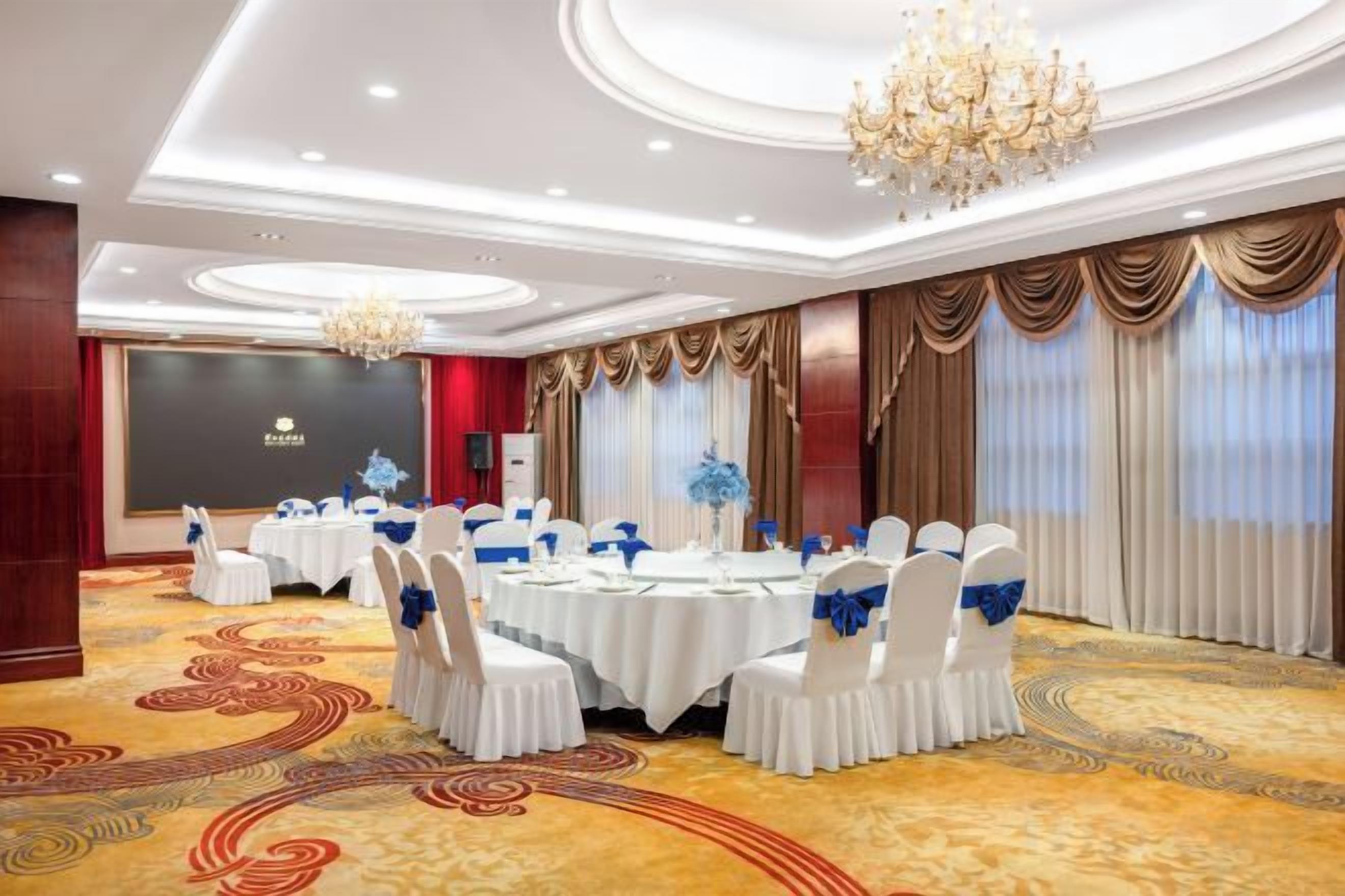 Un salón de banquetes con mesas redondas, sillas blancas y cintas azules.