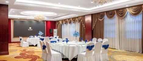 Un salón de banquetes con mesas redondas, sillas blancas y cintas azules.