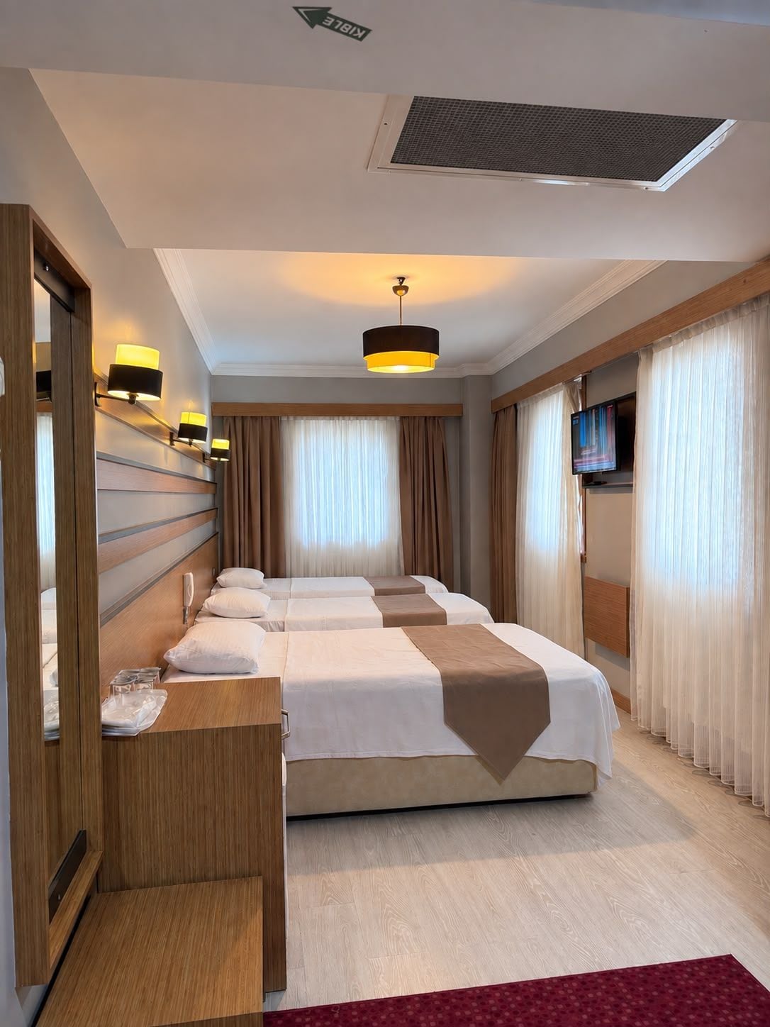 Una habitación de hotel con una cama grande, un escritorio con lámpara, un televisor y una ventana con cortinas.