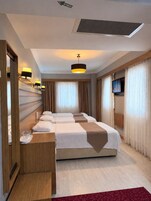 Una habitación de hotel con una cama grande, un escritorio con lámpara, un televisor y una ventana con cortinas.