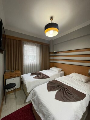 A hotel room with two beds, a desk, a chair, and a television.