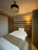 Una habitación de hotel con una cama, un ventilador de techo, una lámpara fijada a la pared y una ventana con cortinas.