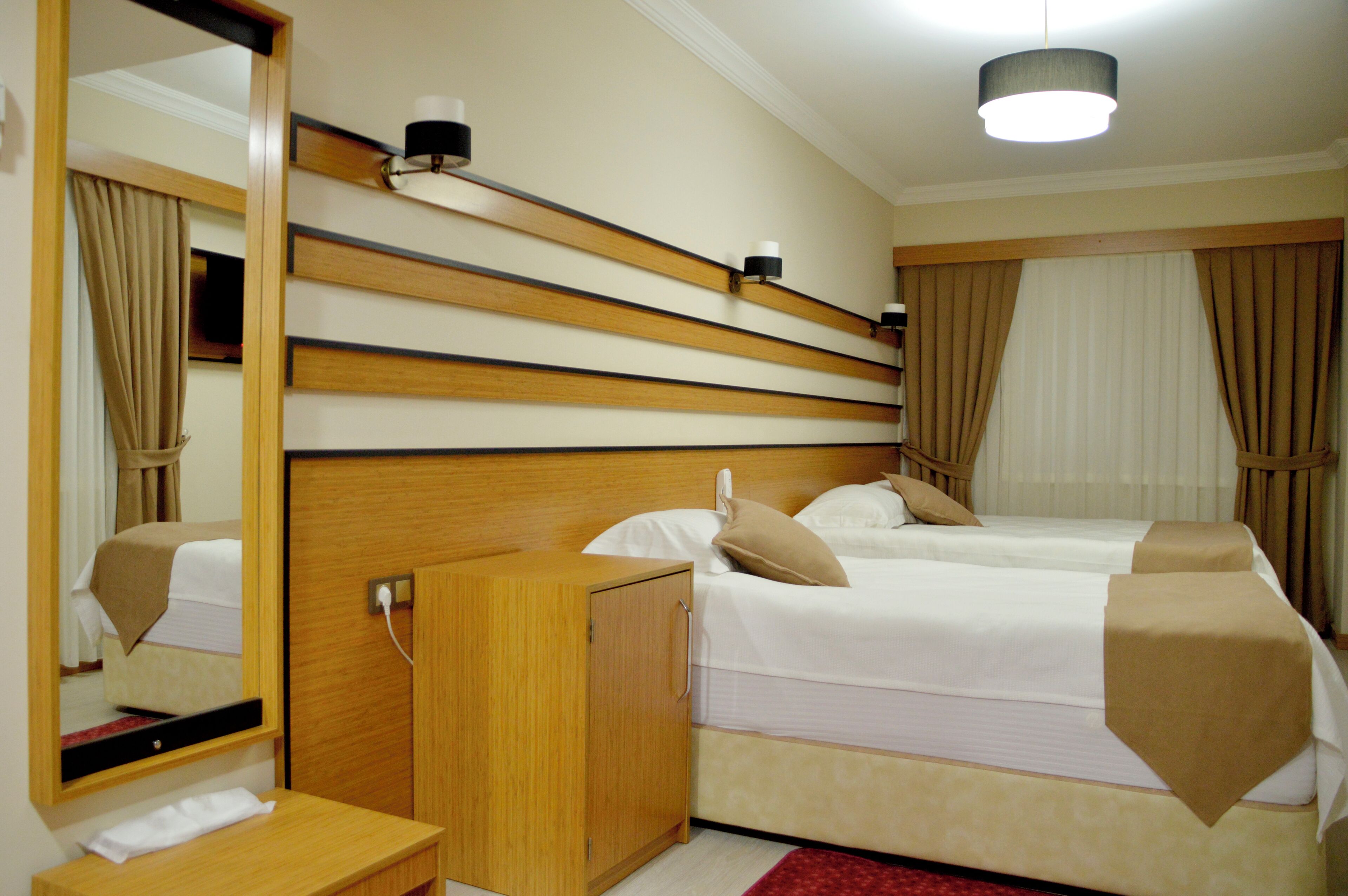 Hotellihuone, jossa on puinen sängynpääty, kaksi sänkyä, yöpöytä, peili ja punainen matto.