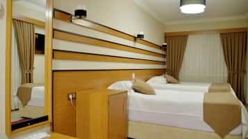 Hotellihuone, jossa on puinen sängynpääty, kaksi sänkyä, yöpöytä, peili ja punainen matto.