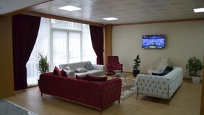 A spacious living room with a large window, a television mounted on the wall, and a red sofa. - Quars Garden Hotel (Düzce)