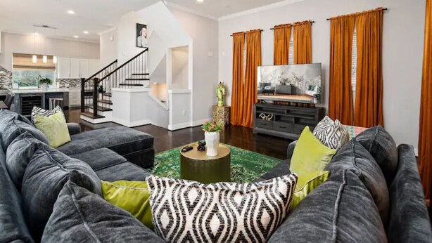 A modern living room with a grey sofa set, a coffee table, and a flat-screen TV. - Centrally Located--Alluring Townhome w/ Engaging Decor & Beautiful Skyline Views (Houston)