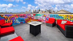 A rooftop lounge with red furniture, a black table, and a colorful graffiti wall. - Centrally Located--Alluring Townhome w/ Engaging Decor & Beautiful Skyline Views (Houston)