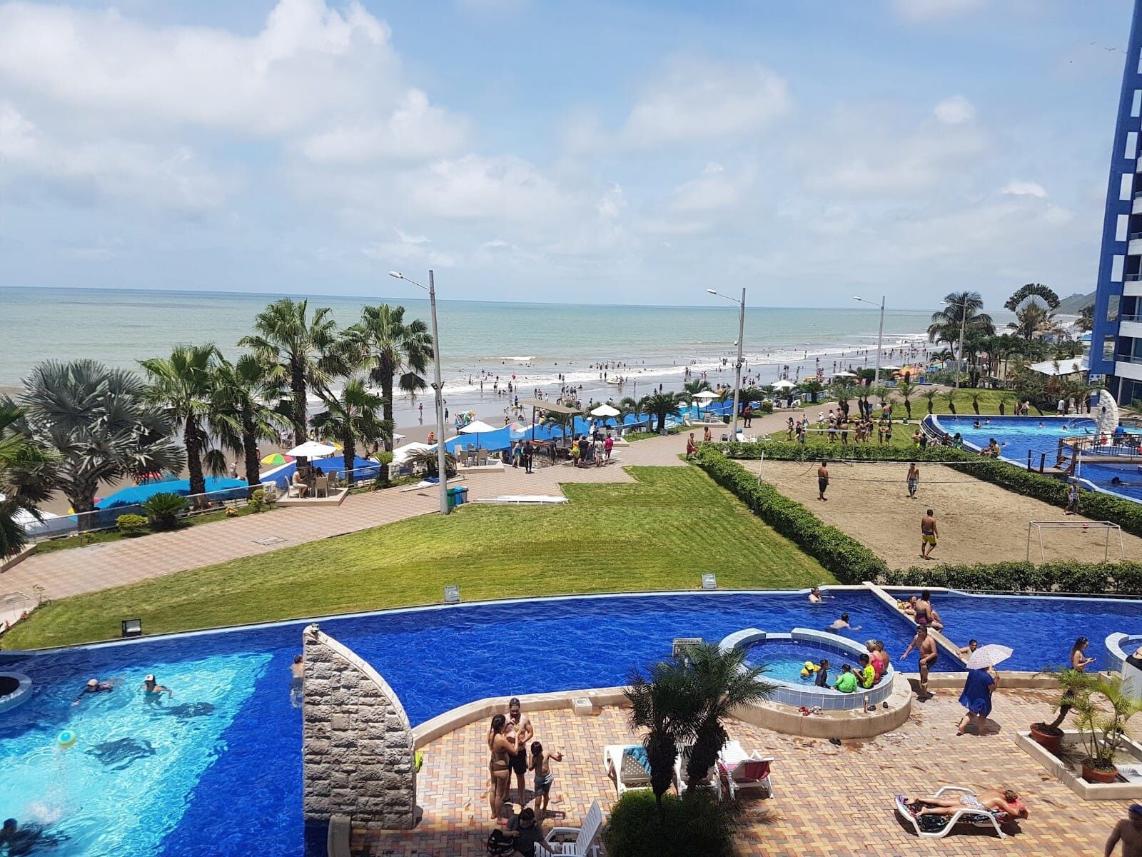 A resort with a large swimming pool, a beach area, and a view of the ocean.