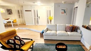 A living room with a sofa, a yellow armchair, a coffee table, and a dining area with a table and chairs. - Beautiful and peaceful Lake house (Inverness)