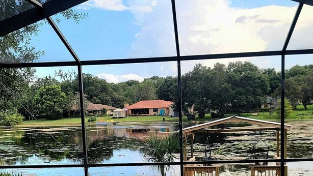 A covered outdoor swimming pool with a view of a pond and surrounding greenery. - Beautiful and peaceful Lake house (Inverness)