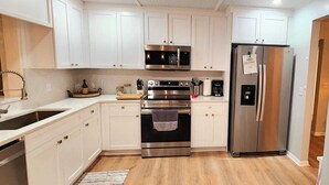 A modern kitchen with white cabinets, stainless steel appliances, and a wooden floor. - Beautiful and peaceful Lake house (Inverness)