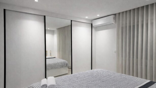 A modern hotel room with a large bed, a mirror, and a window with vertical blinds. - Lovely 1-Bed Apartment in lac1 Tunis (Tunis)