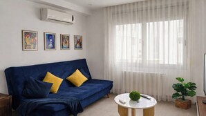 A modern living room with a blue sofa, a round coffee table, and a large window with sheer curtains. - Lovely 1-Bed Apartment in lac1 Tunis (Tunis)