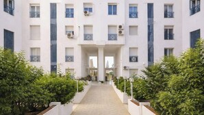 A multi-story building with a central entrance, surrounded by greenery and a tiled pathway. - Lovely 1-Bed Apartment in lac1 Tunis (Tunis)