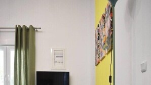 A modern living room with a sofa, a round coffee table with a plant and books, a TV on the wall, and a green curtain. - Pirgos Colorful Studio, Sleeps 2, Parking WiFi Ac (Pirgos Monofatsiou Heraklion)