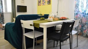 A dining area with a table set for four, chairs, a green tablecloth, and a fruit and drink display. - Pirgos Colorful Studio, Sleeps 2, Parking WiFi Ac (Pirgos Monofatsiou Heraklion)