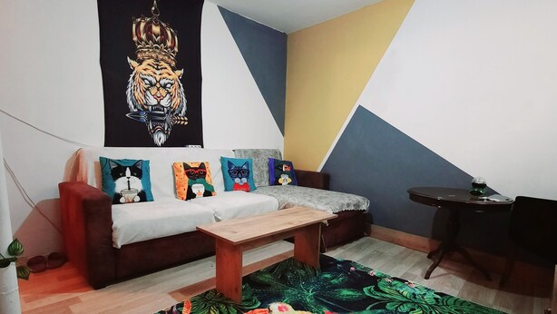 A room with a sofa, a wooden bench, a colorful tiger-themed rug, and a wall with a tiger tapestry. - Lovely 1-Bed Apartment (Istanbul)