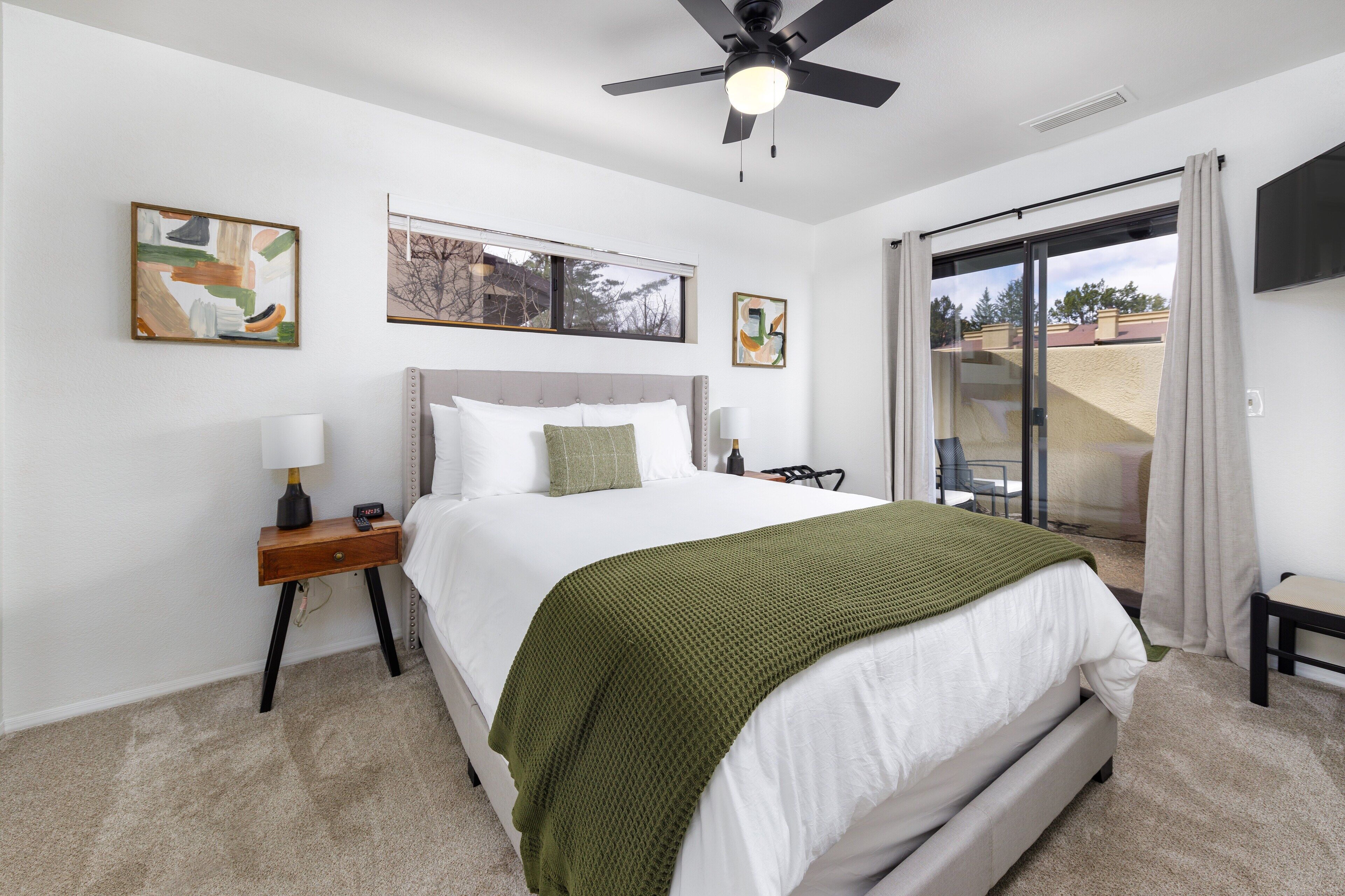 A bedroom with a bed, a nightstand, a ceiling fan, and artwork on the walls.