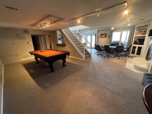 A spacious room with a pool table, a staircase, and a dining area with chairs and a table. - Wasaga Beach cottage  (Wasaga Beach)