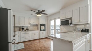 A kitchen with white cabinets, a black refrigerator, a microwave, and a ceiling fan. - Wasaga Beach cottage  (Wasaga Beach)