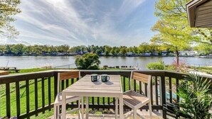 A deck with a table and chairs overlooking a lake, surrounded by greenery and a wooden fence. - Wasaga Beach cottage  (Wasaga Beach)