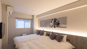 A modern bedroom with a large bed, a mounted air conditioner, a window with blinds, and a wall-mounted artwork. - ONE WORLD Sakaisuji Hommachi (Osaka)