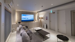 A modern living room with a large flat-screen TV, a sofa, a coffee table, and a lamp. - ONE WORLD Sakaisuji Hommachi (Osaka)