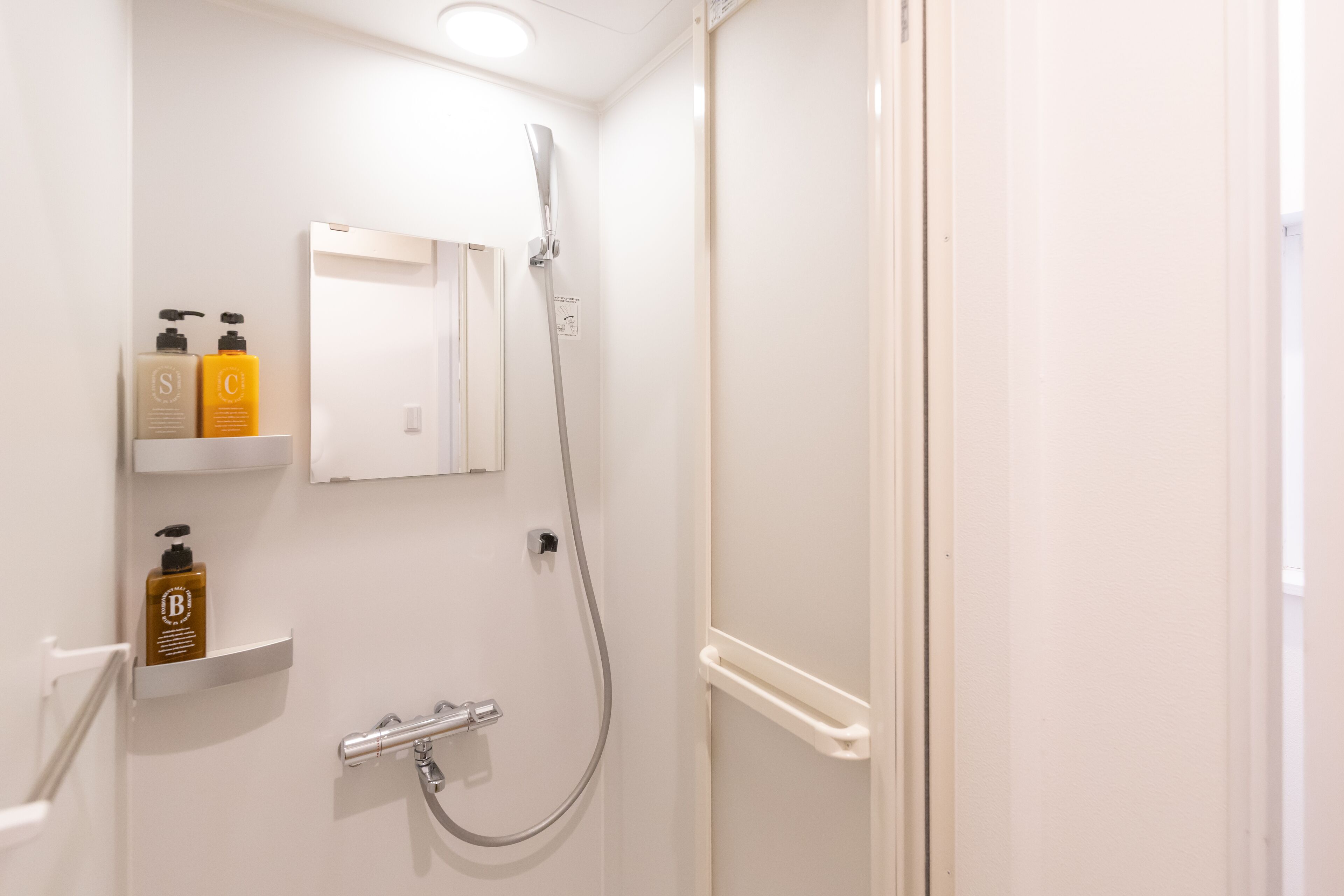 Un baño con ducha, espejo y estantes con artículos de aseo.