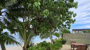A sandy outdoor area with a wooden table and chairs, surrounded by lush greenery and a view of the beach. - Ann's Beach House (Rarotonga)