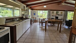 A kitchen with a tiled floor, wooden cabinets, a stove, and a dining area with a table and chairs. - Ann's Beach House (Rarotonga)