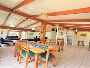 A spacious dining area with wooden tables and chairs, a ceiling fan, and a large window providing natural light.