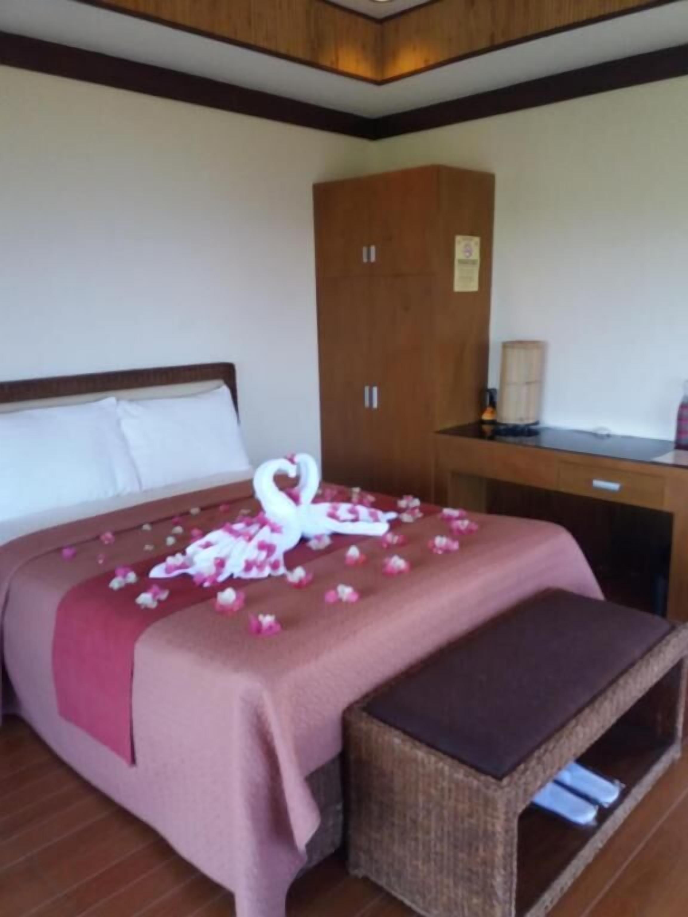 Una habitación de hotel con una cama, un armario de madera, un escritorio y un banco de mimbre.