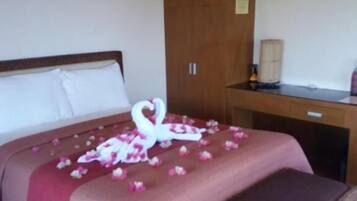 Una habitación de hotel con una cama, un armario de madera, un escritorio y un banco de mimbre.