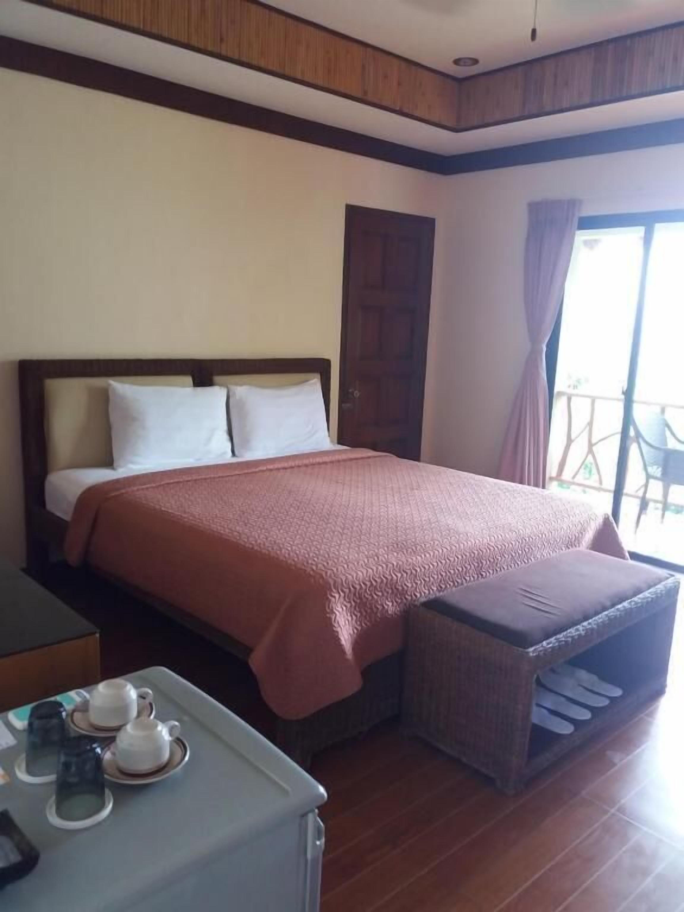 A hotel room with a bed, a small table with tea cups, and a balcony with a chair.