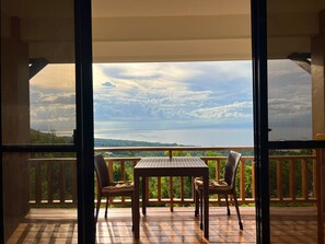 A wooden deck with a table and two chairs, overlooking a scenic view of a body of water and distant land. - Infinity Heights Resort (Siquijor)