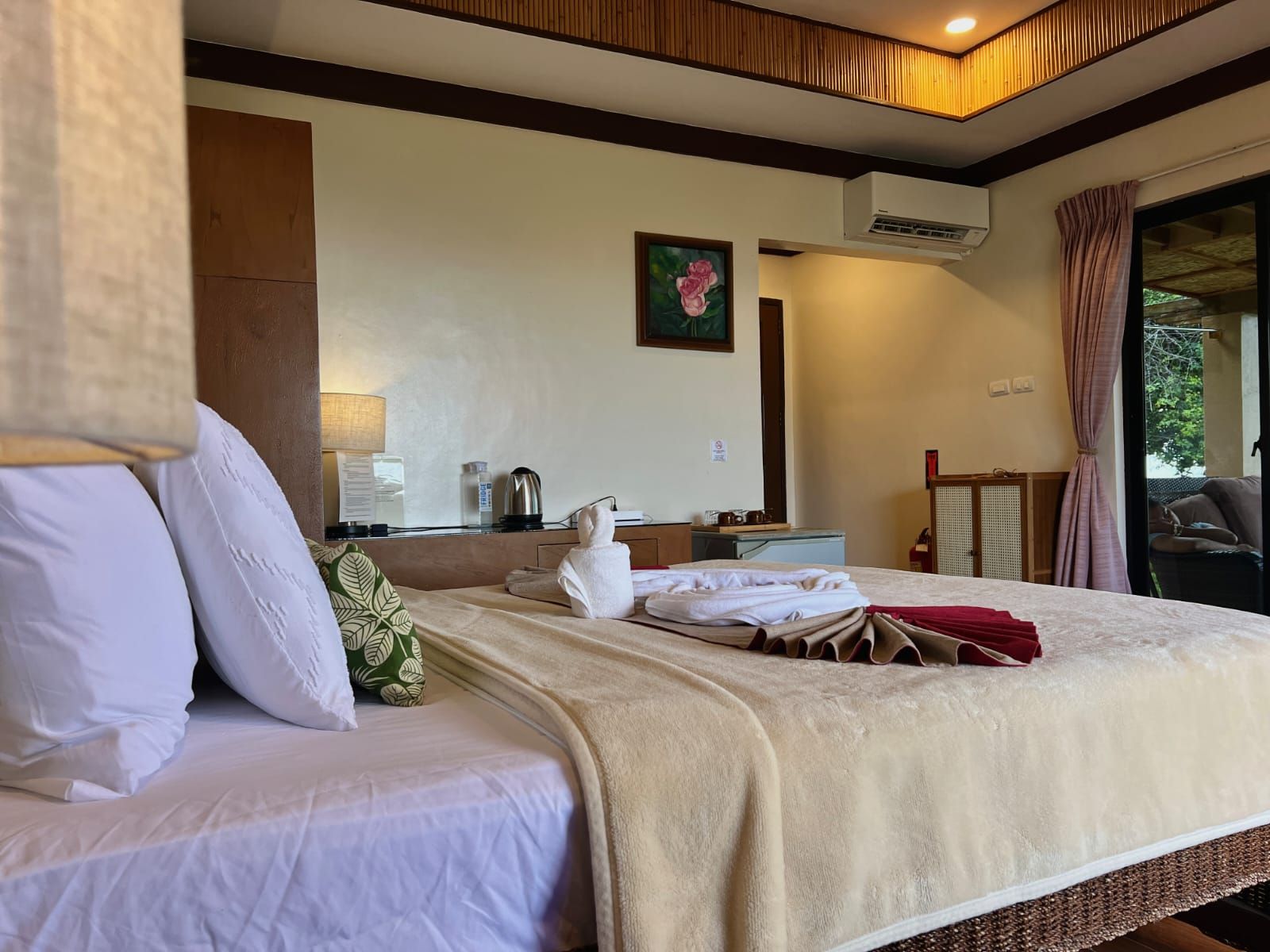 A hotel room with a bed, a bedside table, a lamp, a painting, and a window with curtains.