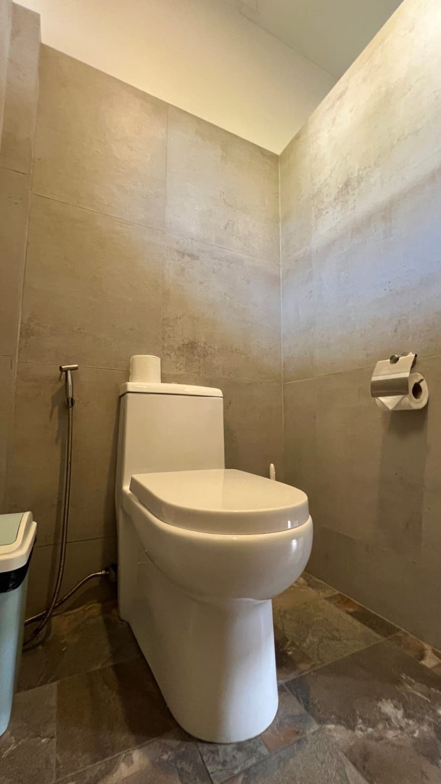 Un baño con inodoro, ducha y un dispensador de papel higiénico en la pared.