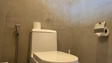 Un baño con inodoro, ducha y un dispensador de papel higiénico en la pared.