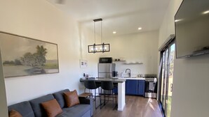 A modern kitchen with a central island, a dining area with chairs, and a living room with a sofa and a painting.