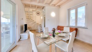 A modern dining area with a glass table, white chairs, and a staircase in the background. - Golden Terrace Leggiuno 2BR/2BA Walk to the Lake, Leggiuno, Italy (Leggiuno)