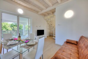 A modern living room with a glass dining table, white chairs, a brown leather sofa, a flat-screen TV, and a staircase leading to an upper level. - Golden Terrace, Leggiuno, Italy (Leggiuno)