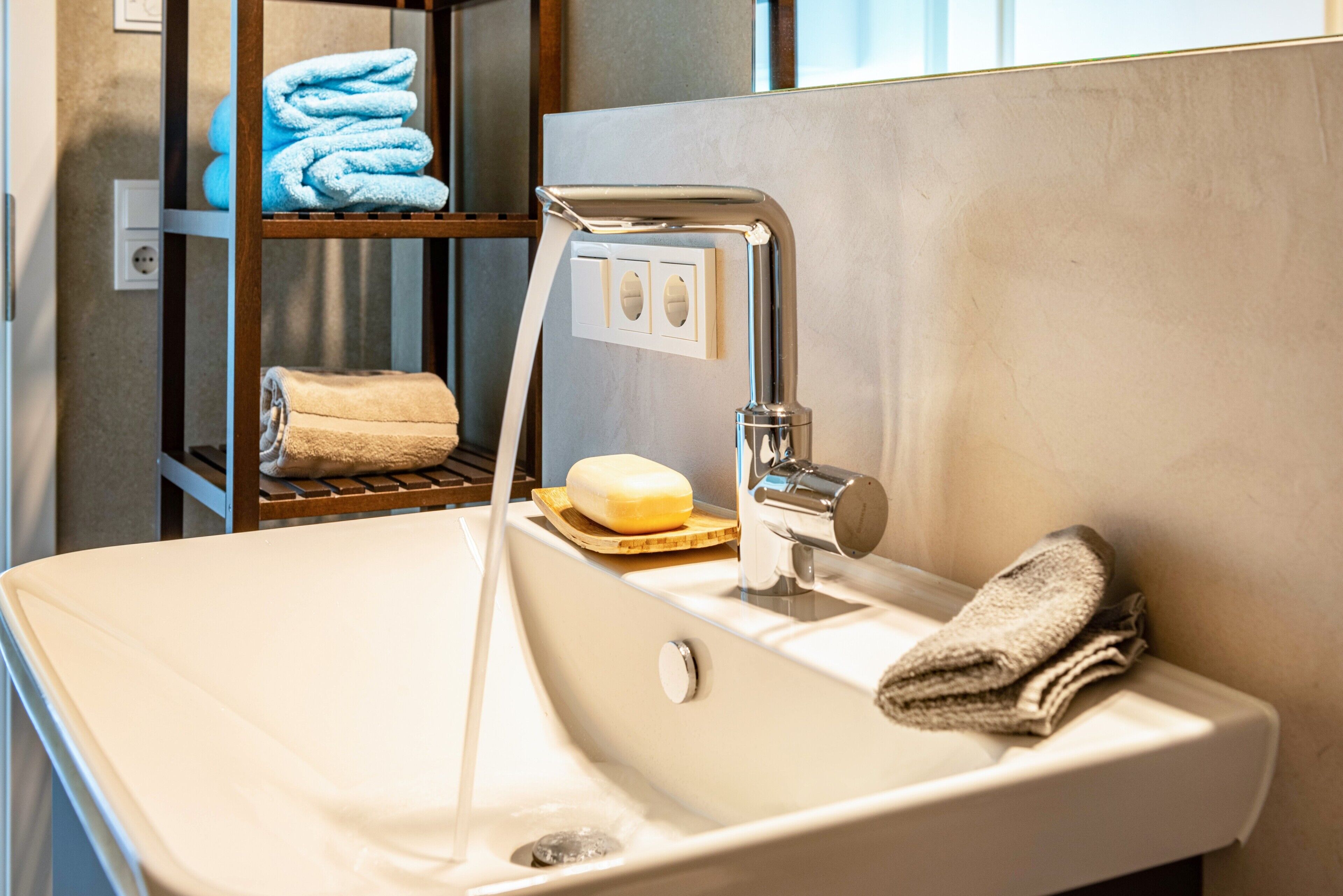 Une salle de bain avec un lavabo blanc, un robinet chromé et une étagère où sont pliées des serviettes.