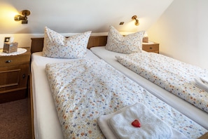 Un lit double avec une literie à motifs floraux, des tables de chevet avec des lampes et une petite horloge de chevet.