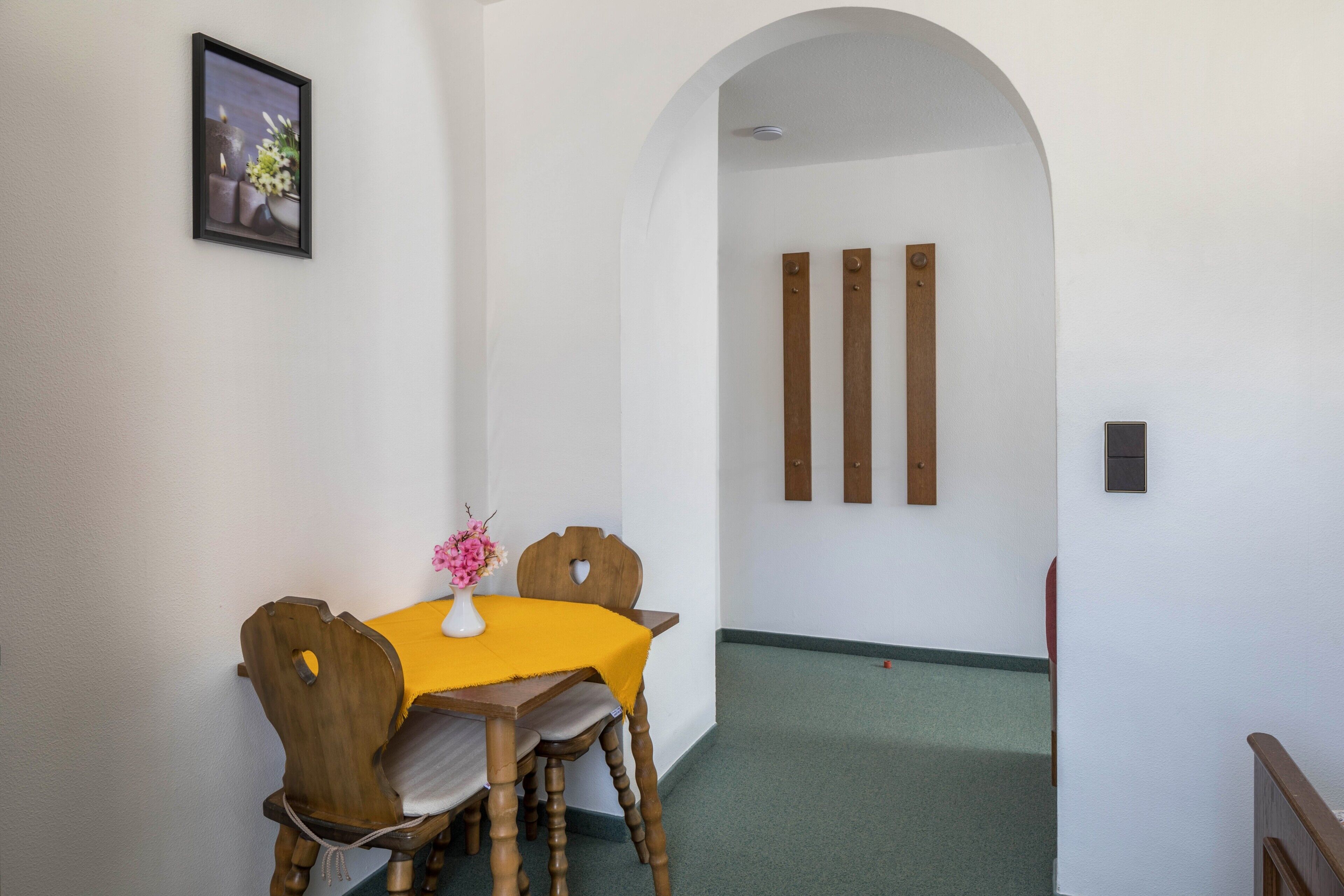 A dining area with a table, chairs, a vase with flowers, and a picture on the wall.